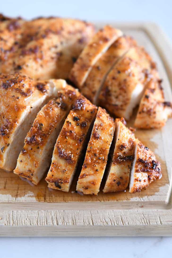 Sliced cooked chicken breasts on wood cutting board.
