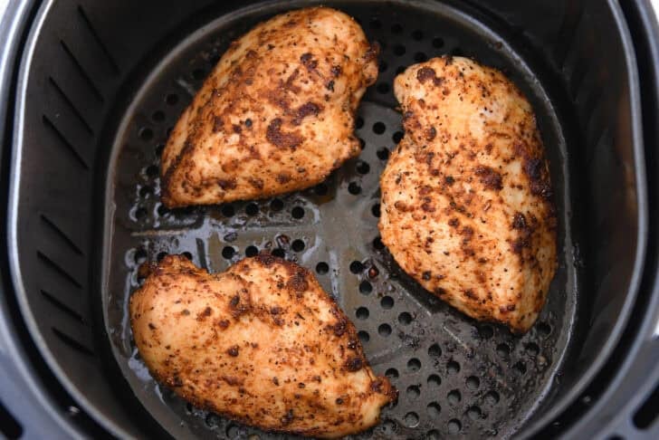 Three cooked chicken breasts in basket of air fryer.