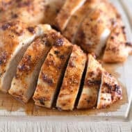 Sliced cooked chicken breasts on wood cutting board.