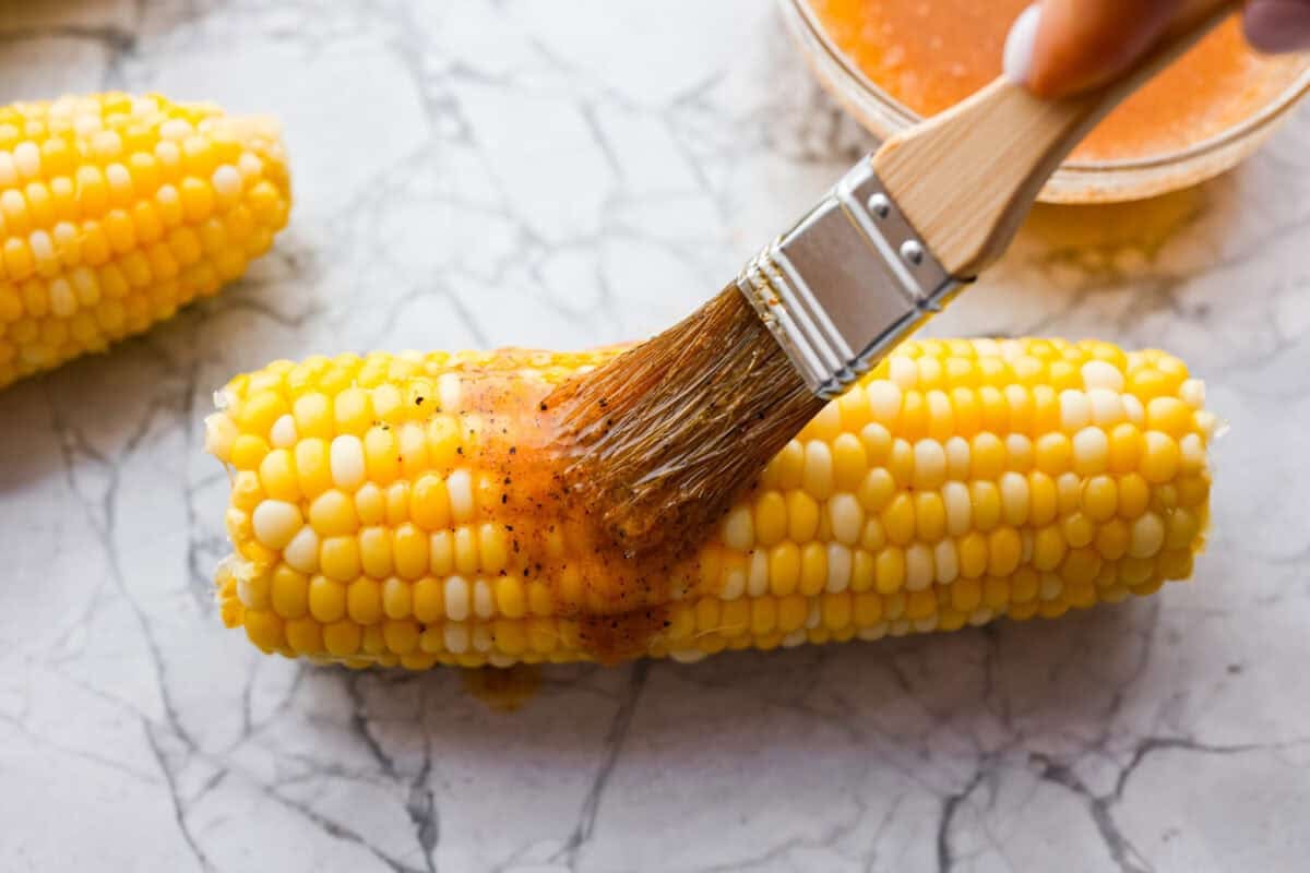 Someone basting a cob of corn with the seasoned butter. 