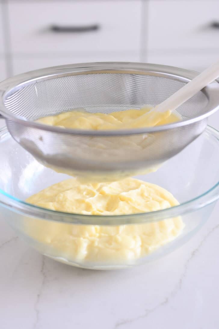 Straining vanilla pudding through fine mesh strainer into glass bowl.