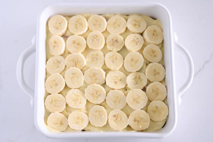 White square 8X8 baking dish with sliced bananas over the vanilla pudding.