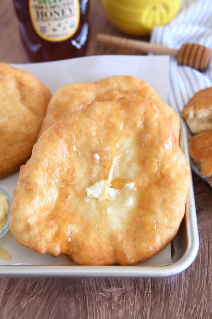 Several pieces of warm fry bread on baking tray with butter and honey.