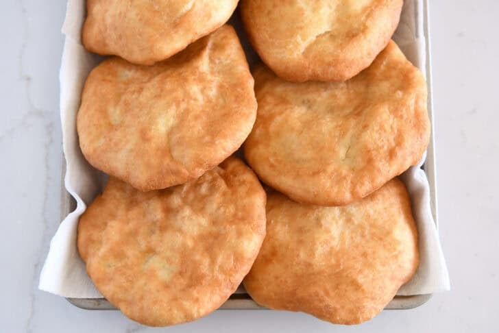 Six pieces of cooked fry bread on paper towel lined baking sheet.