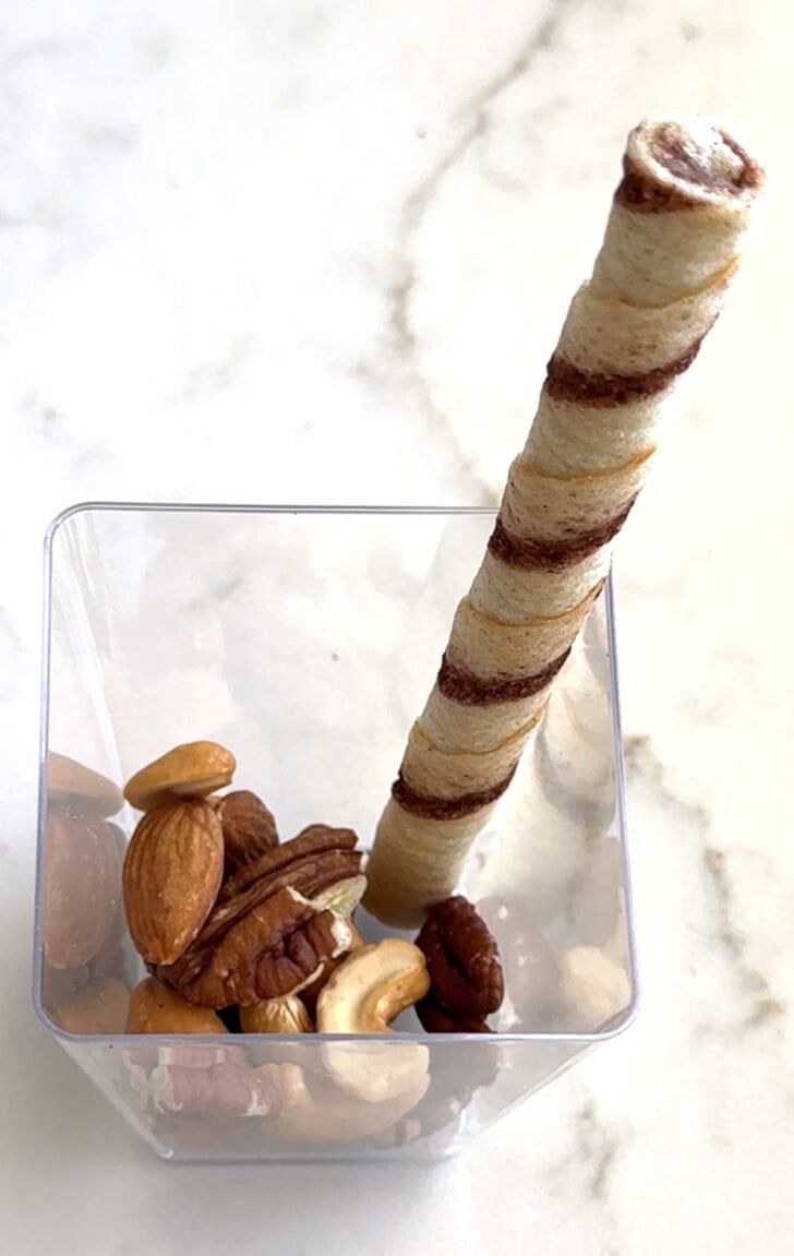 Square plastic cup with nuts and pirouline.