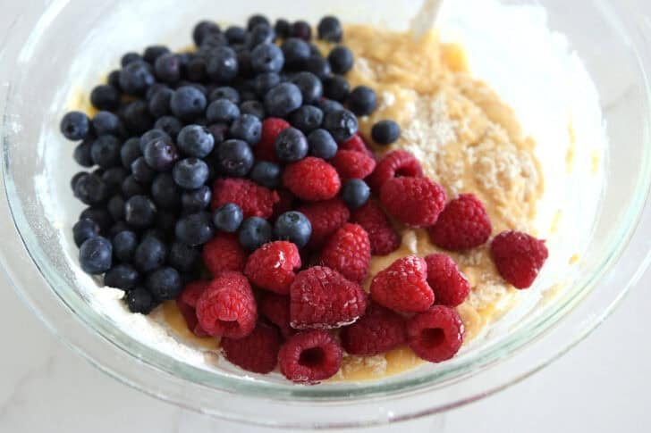Glass bowl with cake batter, fresh blueberries and fresh raspberries.