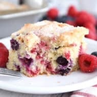 Piece of berry cake on white plate with bite taken out with fresh raspberries on the plate.