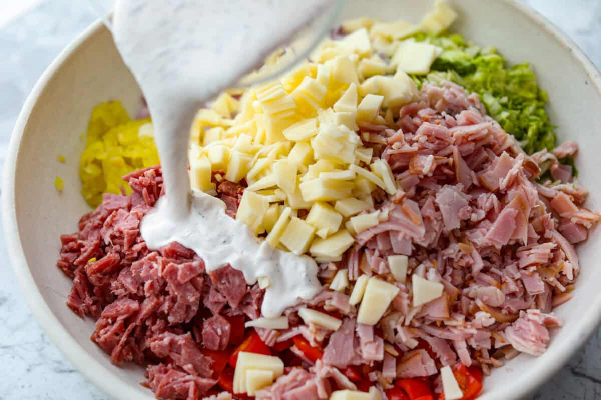 Dressing being poured over the sub in a tub dip ingredients. 