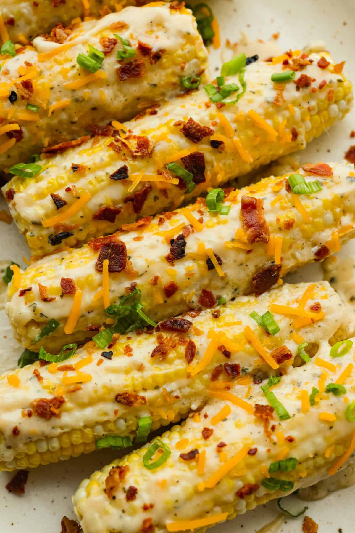 Crack corn on the cob on a serving platter, covered in green onions and bacon.