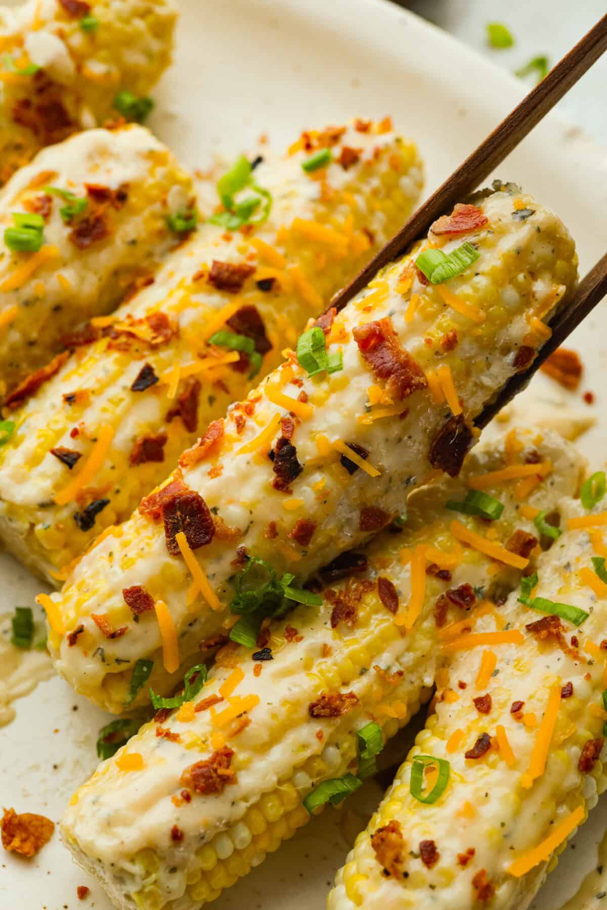 Someone picking up a crack corn on the cob with wooden tongs. 