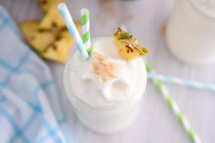 Top down view of tall glass cup with frozen piña colada, toasted coconut, a triangle of fresh pineapple and a bit of toasted coconut on top.