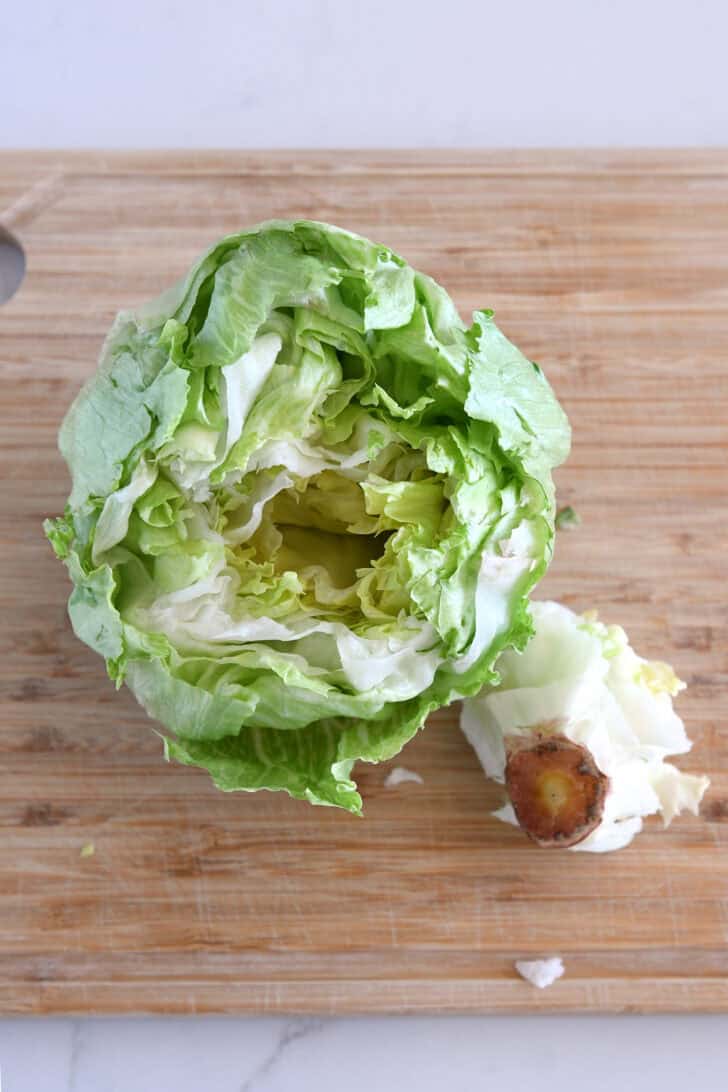 Wood cutting board with cored head of iceberg lettuce.
