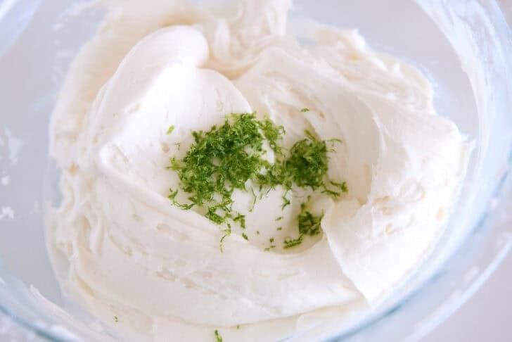 Glass bowl with mixed coconut lime frosting and fresh lime zest.