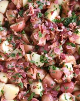 Top down view of a white oval dish with potato chunks, bacon pieces, and chopped parsley.