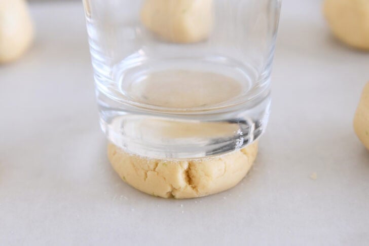 Pressing sugar cookie dough ball into thick disc with sugared bottom drinking glass.