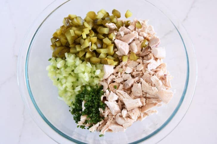 Glass bowl with chopped chicken, chopped green onions, chopped celery, and chopped dill pickles.
