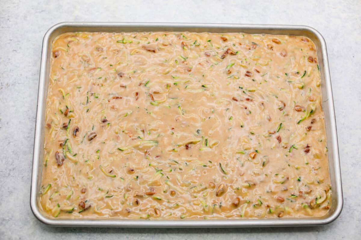 Zucchini bars batter spread out in a jelly roll pan. 