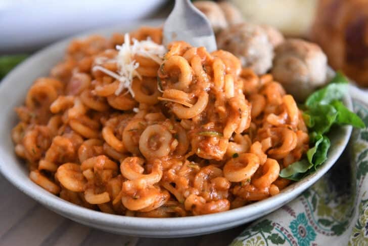 Saucy pasta with shredded zucchini piled high on plate with fork scooping bite.