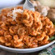 Saucy pasta with shredded zucchini piled high on plate with fork scooping bite.