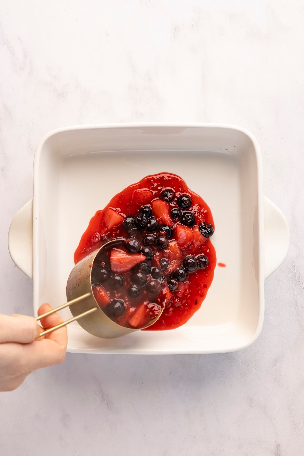 Pouring 1 cup berry mixture into an 8-inch square pan.