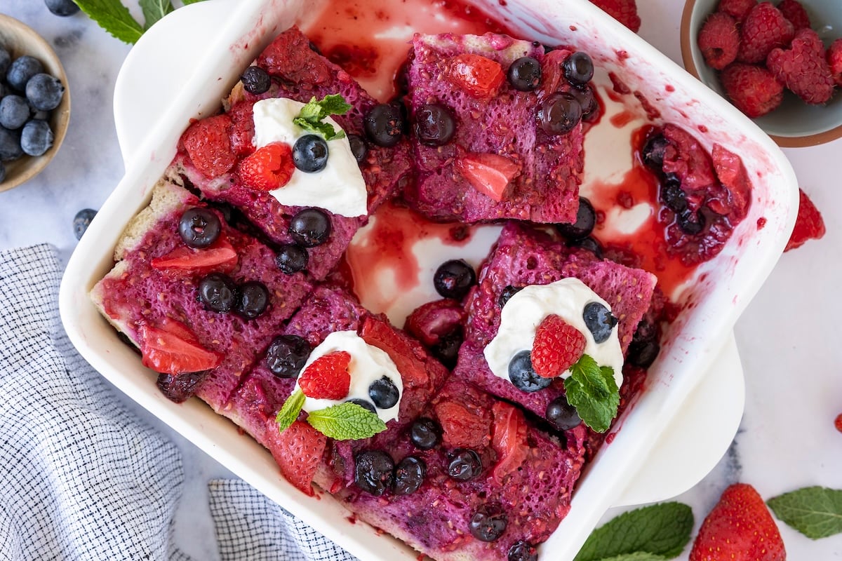 8-in square pan with Summer Berry Pudding cut into squares and topped with dollops of whipped cream and mint