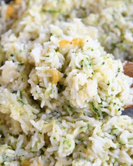 A wooden spoon taking a large scoop of cheesy rice out of a pot.