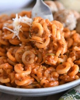 Saucy pasta with shredded zucchini piled high on plate with fork scooping bite.