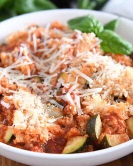 Serving of chicken zucchini Italian skillet in white bowl with parmesan cheese and fresh basil.