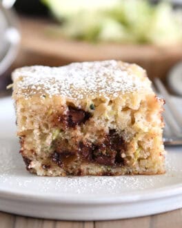 Square of zucchini chocolate chip cake dusted with powdered sugar on gray plate.
