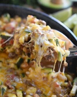 serving spoon lifting up cheesy portion of zucchini skillet