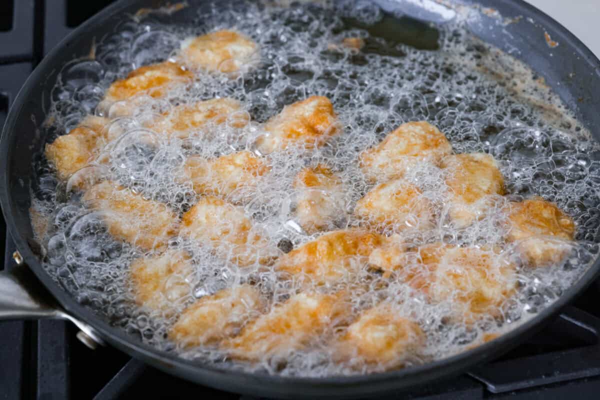 Coated chicken pieces frying in oil in a skillet.