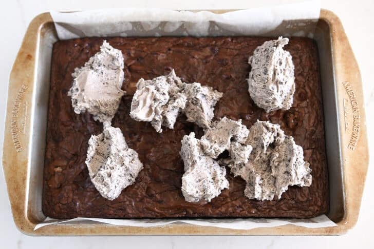 Baked pan of brownies with Oreo frosting dolloped on top.