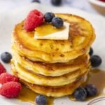 white plate with stack of cottage cheese pancakes topped with maple syrup, butter, and berries
