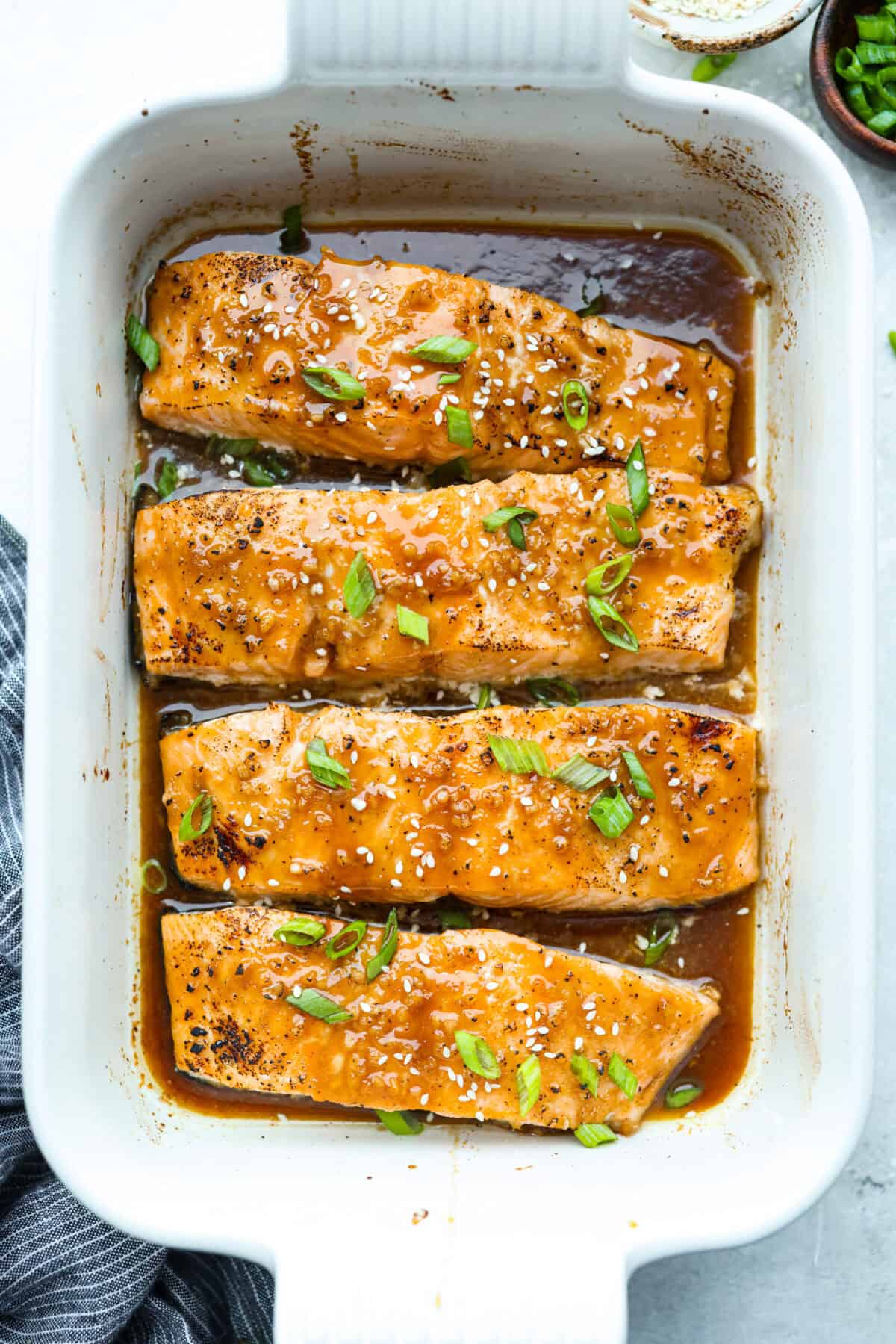 Overhead shot of 4 maple glazed salmon fillets cooked and garnished with sesame seeds and green onions. 