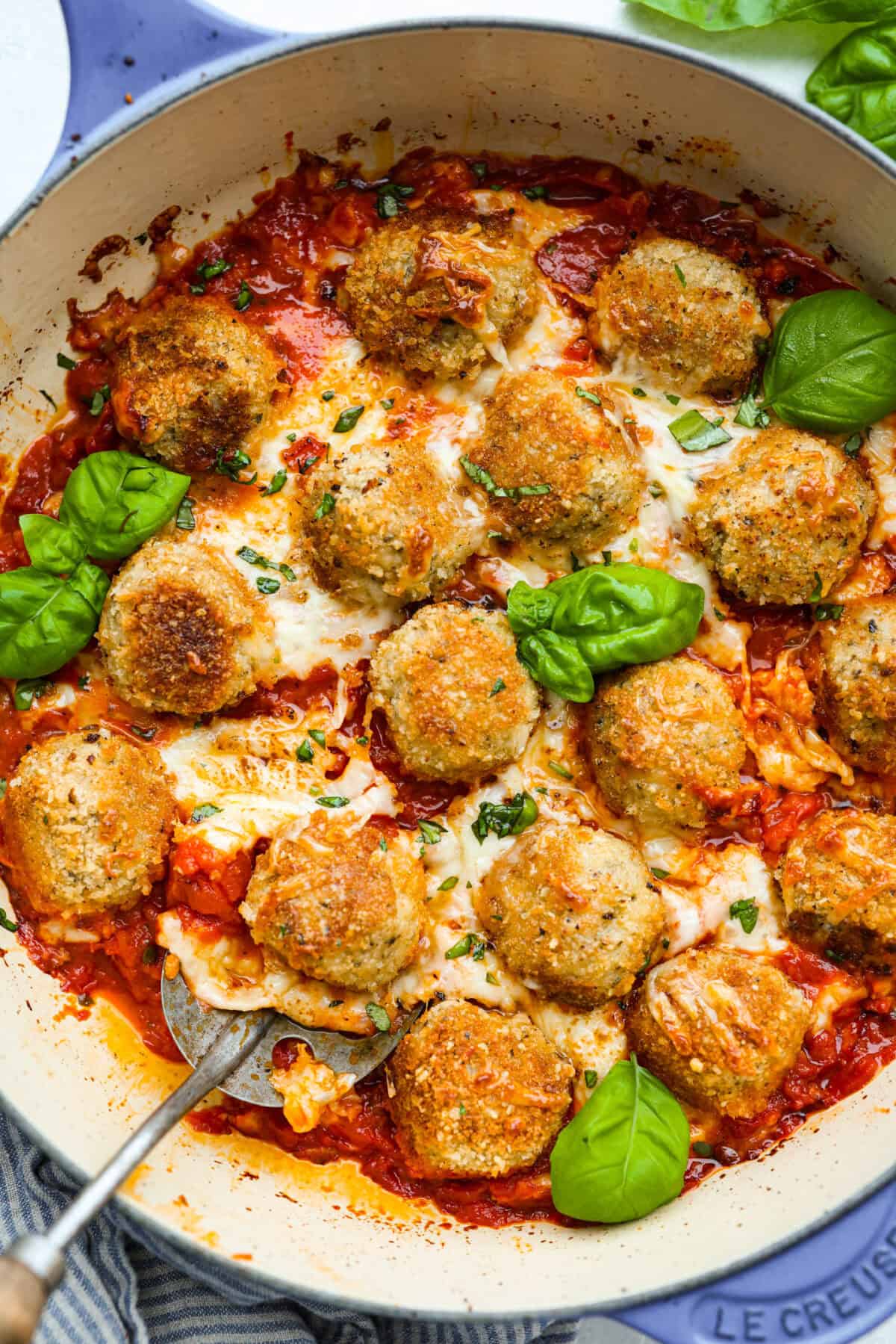 Chicken Parmesan meatballs cooked and baked in a skillet, with melty cheese and garnished with fresh basil. 
