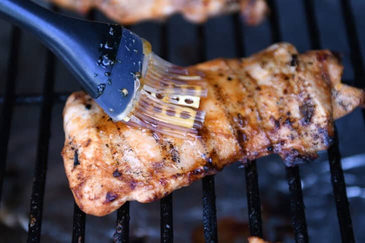 Brushing honey garlic sauce on grilled chicken.