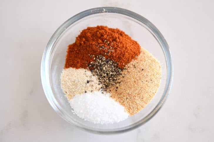 Glass bowl with smoked paprika, onion powder, garlic powder, salt and pepper.