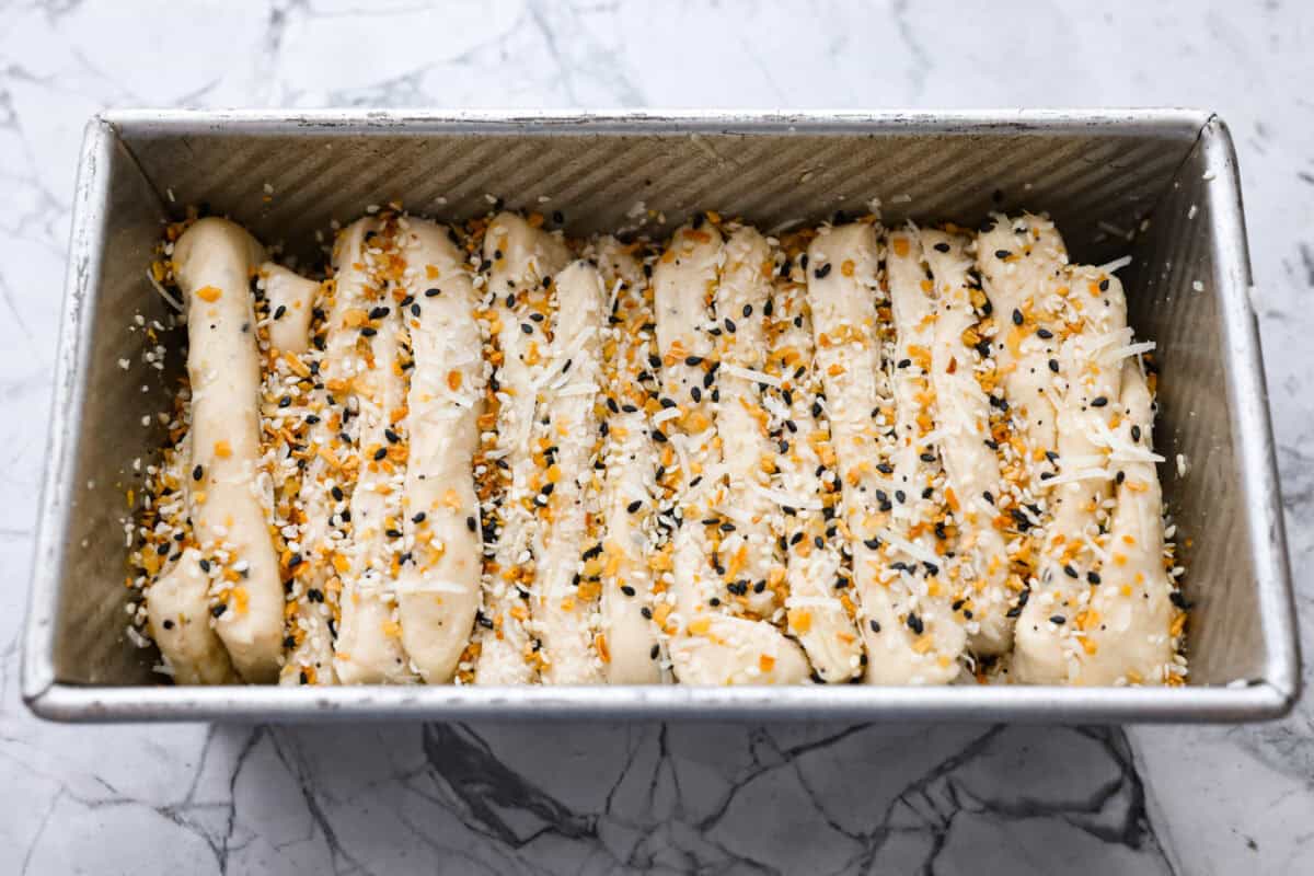 Dough stacks added to the loaf pan and topped with more everything bagel seasoning and cheese. 
