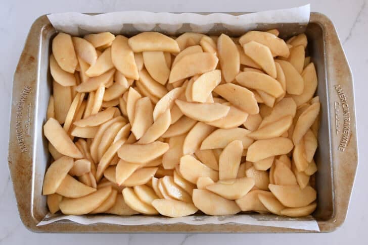 Metal 9X13-inch pan filled with sliced apples mixed with caramel and cinnamon.