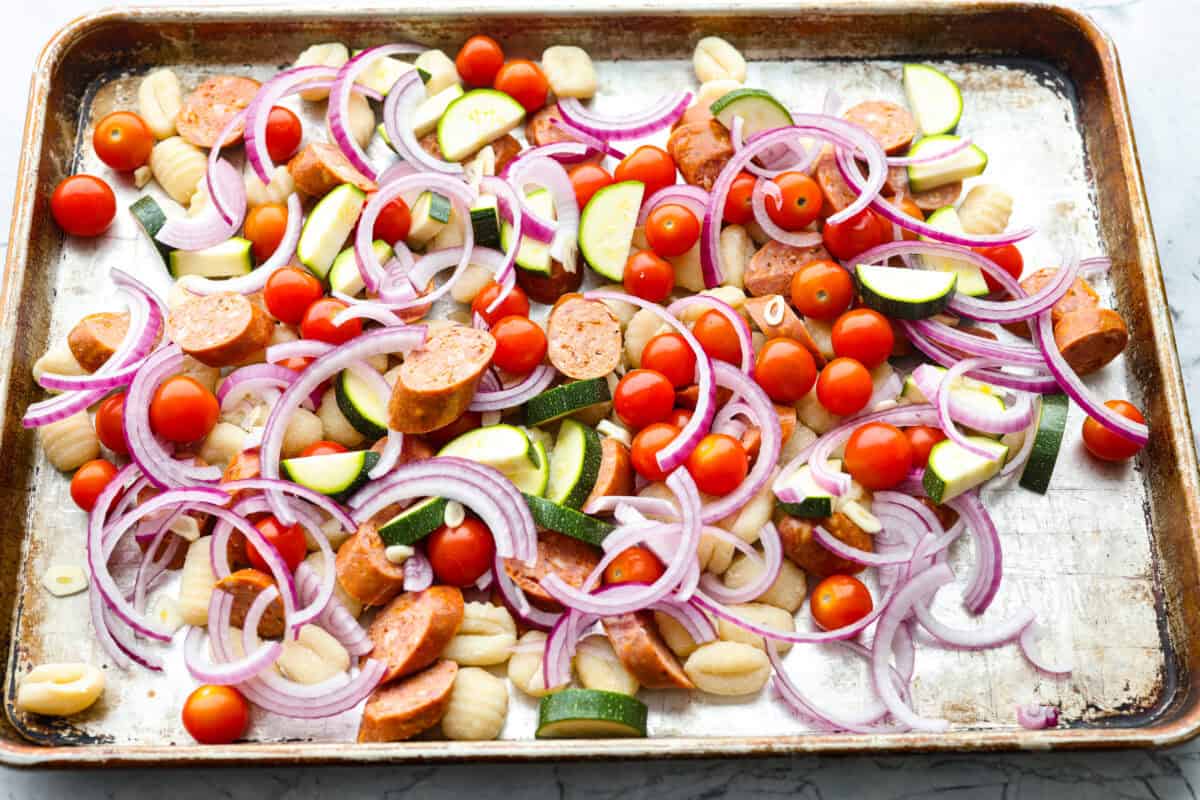 Veggies, gnocchi, and sausage spread out on a sheet pan. 