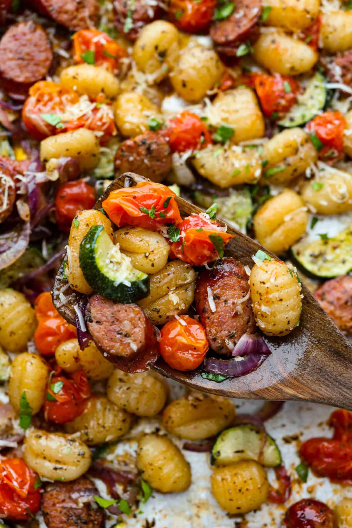 Close up of a scoop of sheet pan gnocchi on a wooden spoon. 
