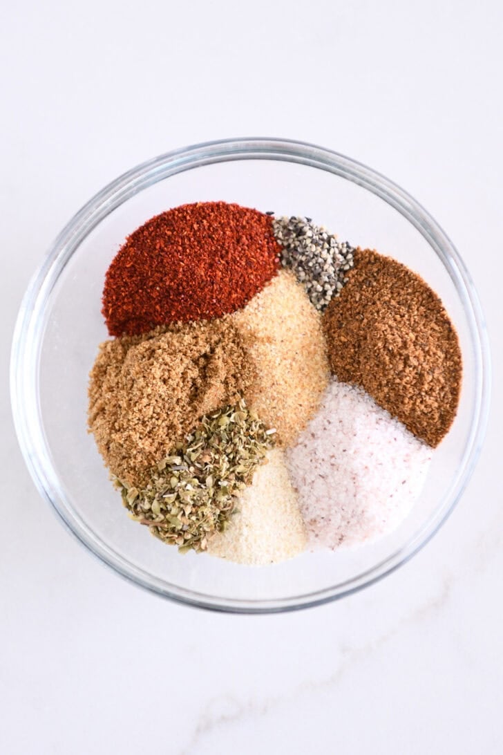 Glass bowl with chili powder, cumin, paprika, garlic powder, onion powder, oregano, salt and pepper.