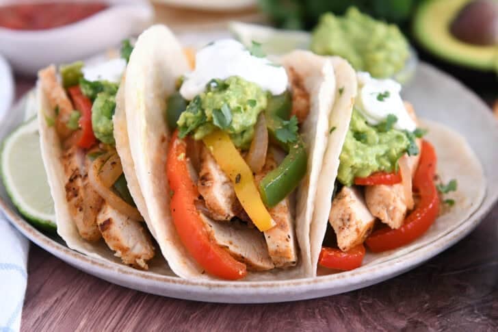 Three flour tortillas filled with sliced, cooked chicken, bell peppers, onions, guacamole and sour cream.