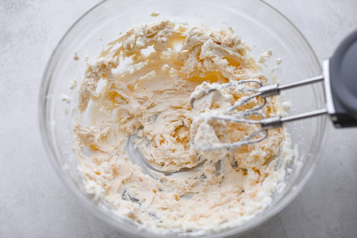 Cream cheese being beaten with a hand mixer. 