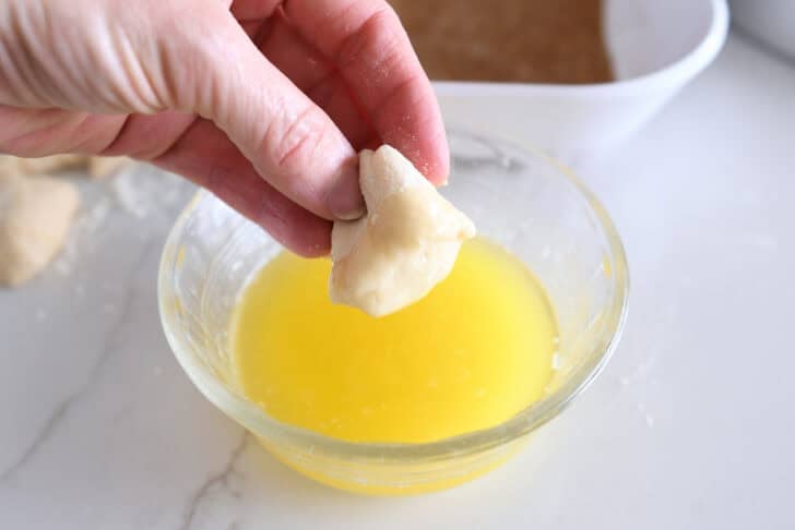 Dipping small piece of roll dough in melted butter.