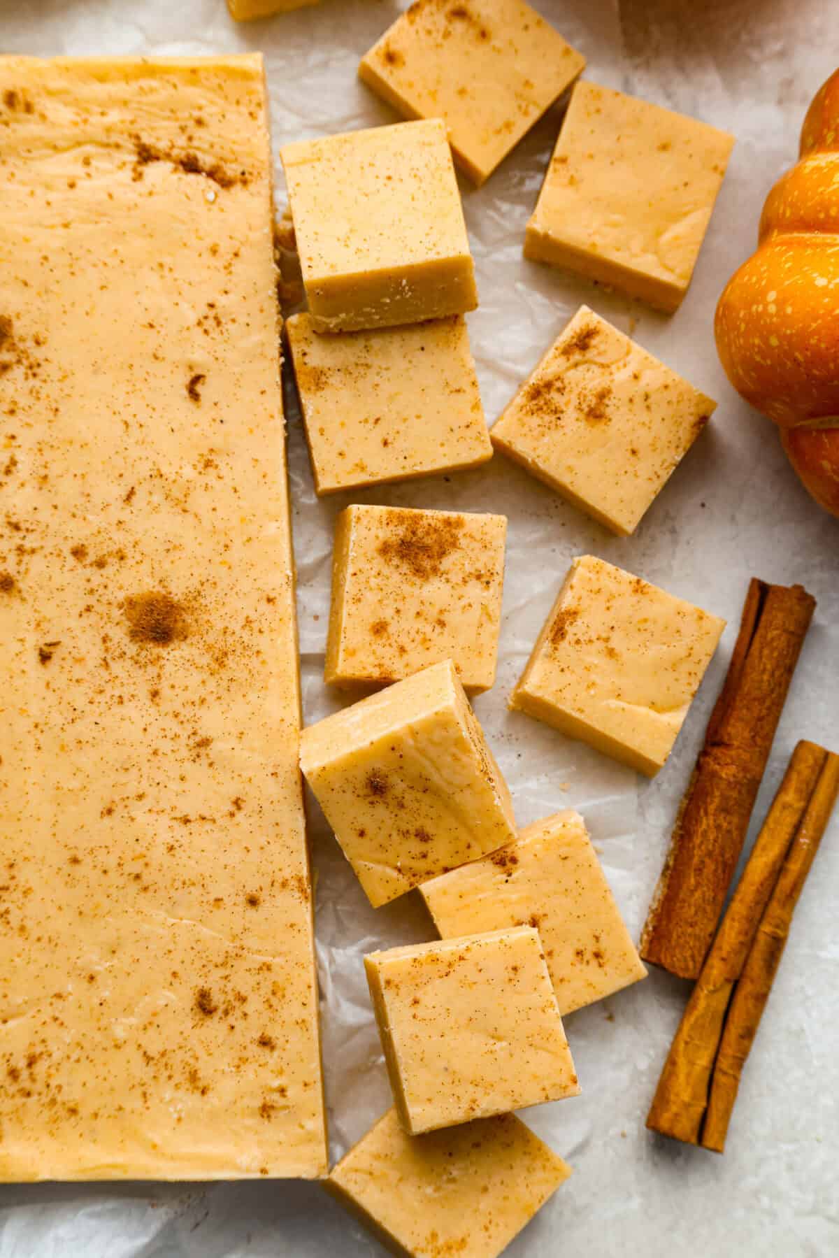 Overhead shot of pumpkin fudge cut into squares with sticks of cinnamon next to them. 