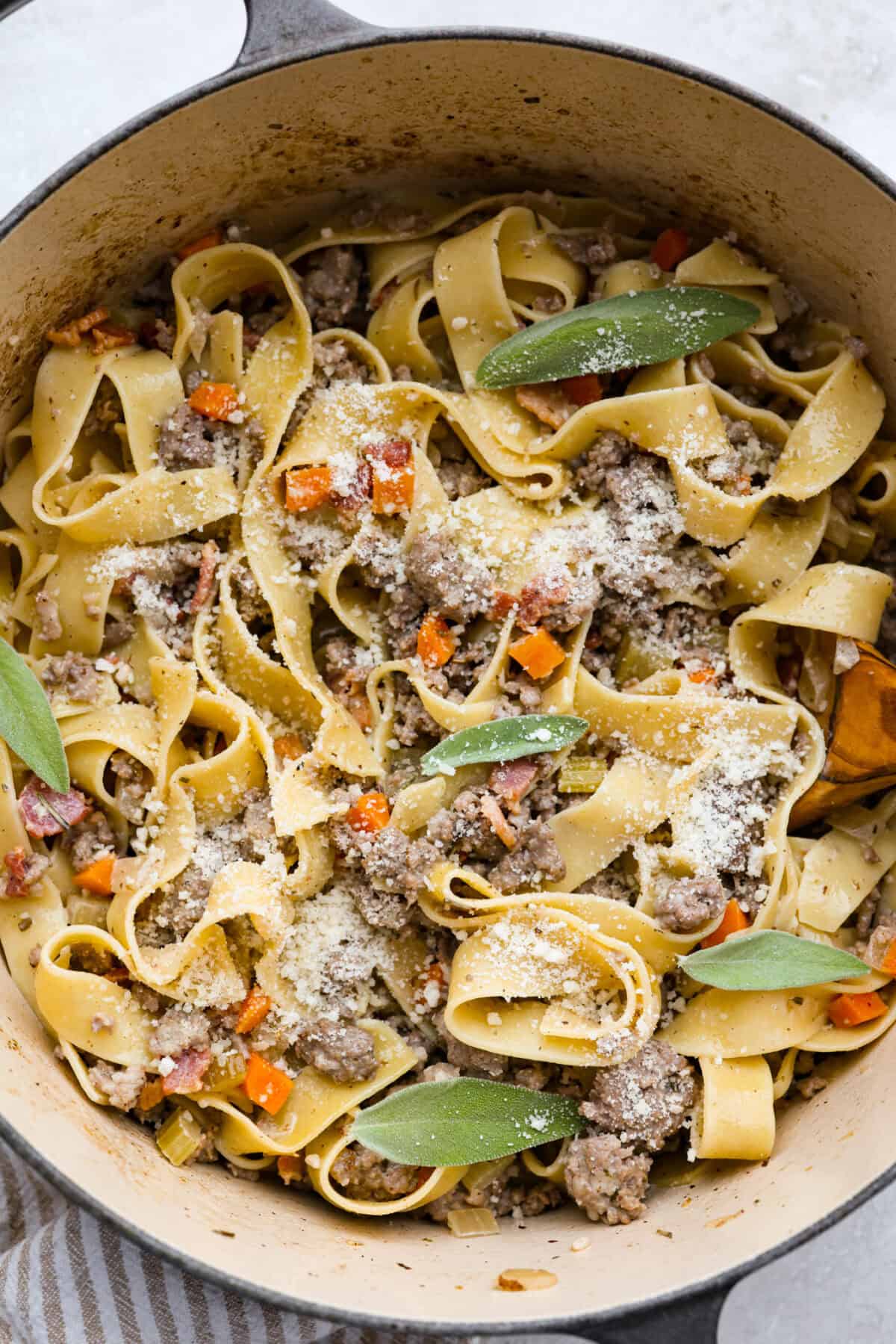 Pot of white bolognese sprinkled with parmesan cheese and sage leaves. 