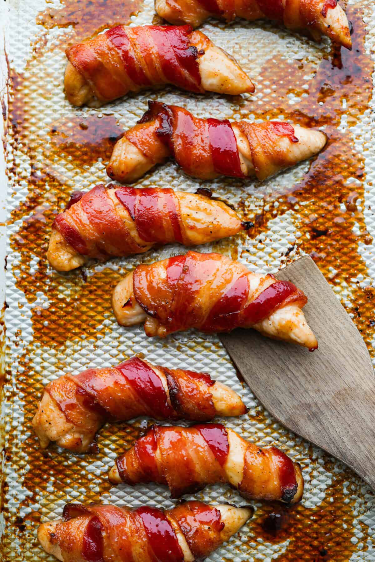 Bacon brown sugar chicken tenders cooked and on a baking rack with a wooden spatula. 