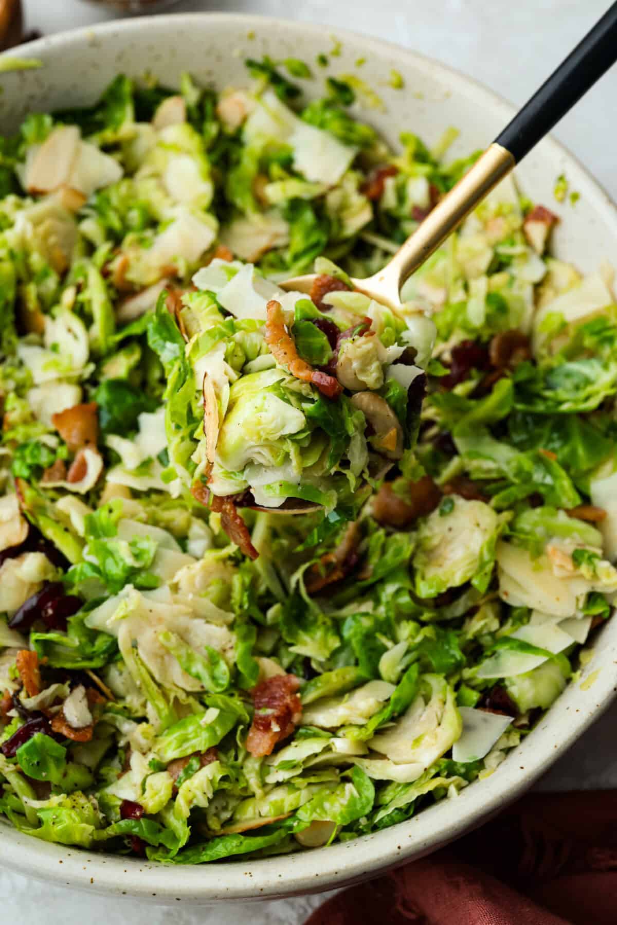 Someone lifting a large spoonful of warm Brussels sprouts salad with bacon out of the large serving bowl. 
