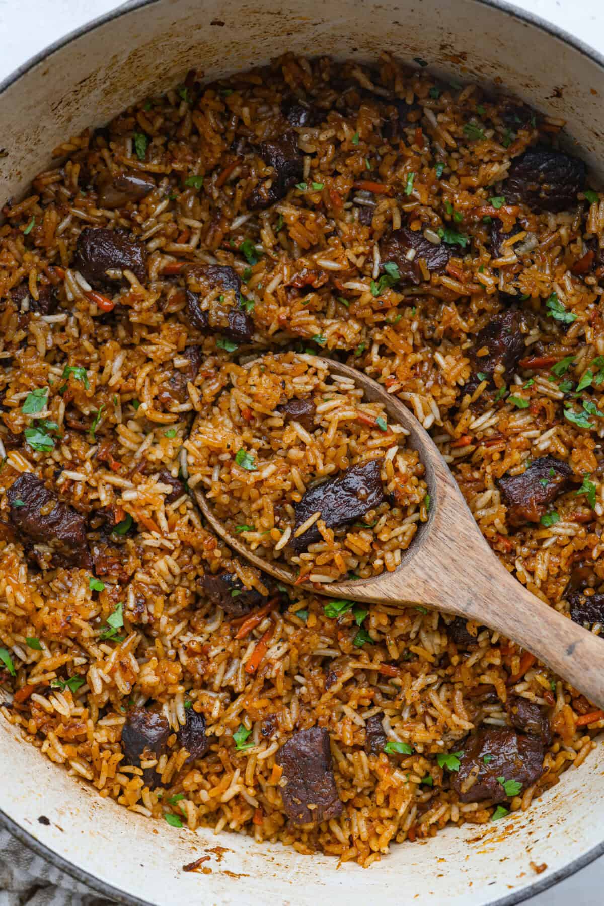 Dutch oven with one pot beef and rice all cooked with a large wooden serving spoon. 